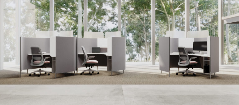 Office space with several modern cubicles in front of floor to ceiling windows with large trees outside.