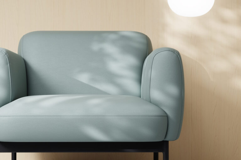 A light blue chair in front of a light wood wall with a round light above the chair.