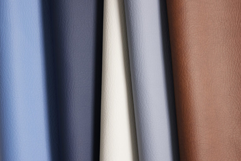 A leather-like material in various colors such as blue, white, and natural leather draped over each other with a visible grain texture visible on the surface of the material.