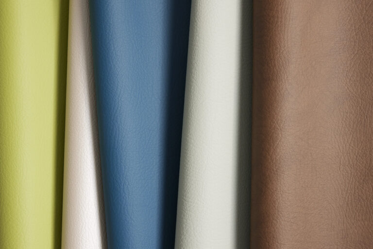 A leather-like material in various colors such as blue, green, and natural leather draped over each other with a visible grain texture visible on the surface of the material.