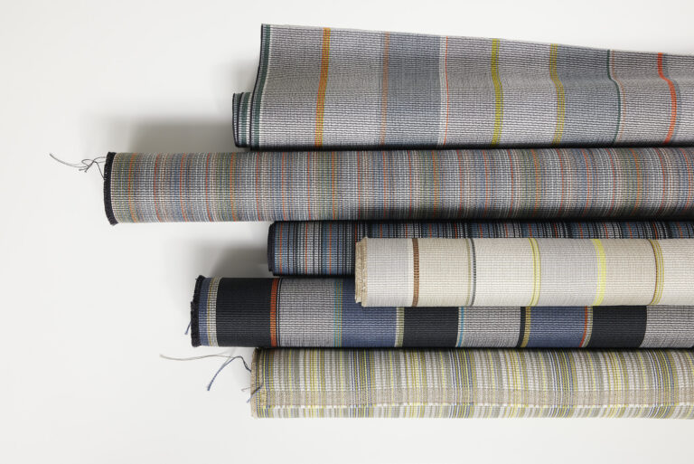 Rolls of multi-colored striped textiles stacked on top of each other on a white background.