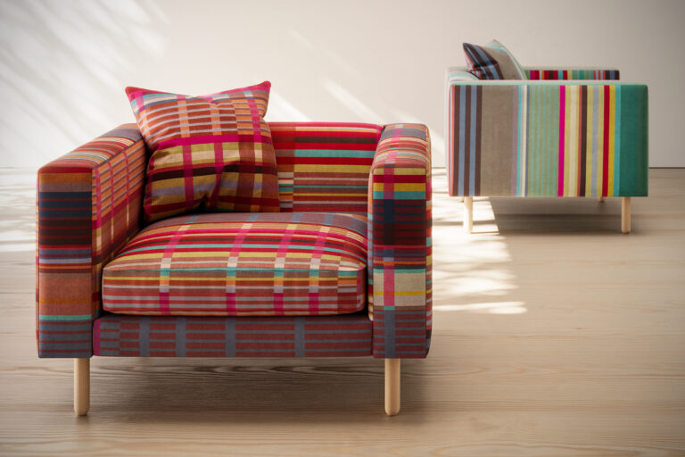 Two lounge chairs in colorful stripe patterns in a white room with a wood floor.
