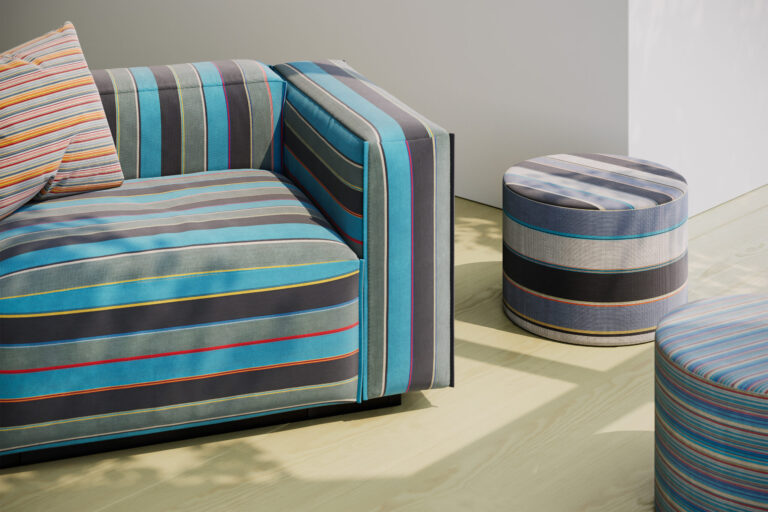 A lounge chair in a bold stripe next to two round ottomans, also with stripe patterns in a white room with wood floors.